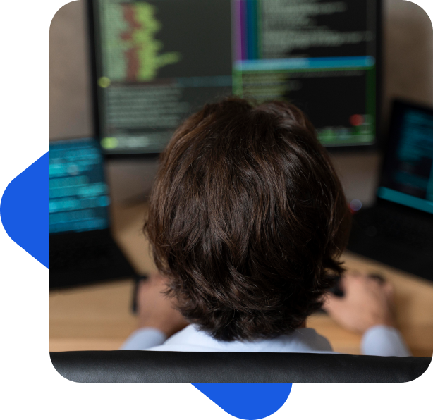 faq-pentesting Persona de espaldas utilizando múltiples pantallas de ordenador con códigos de programación visibles.